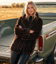 Load image into Gallery viewer, A woman wearing a brown leopard-print faux fur coat leans against the tailgate of a vintage green pickup truck in an outdoor field.
