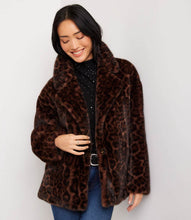 Load image into Gallery viewer, A woman wearing a brown faux fur leopard print coat over a black embellished top and blue jeans, posing against a light gray background.