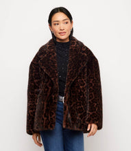 Load image into Gallery viewer, A woman modeling a brown and black leopard-print faux fur jacket over a black embellished top and blue jeans, photographed against a plain white studio background.