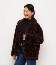 Load image into Gallery viewer, A woman wearing a brown faux fur leopard-print jacket over a black top and blue jeans, standing against a plain white background.