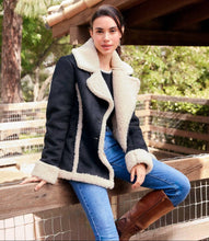 Load image into Gallery viewer, Woman wearing a black coat with off-white fur trim, black top and brown boots sitting on a wooden bench outdoors.