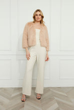Load image into Gallery viewer, Woman wearing a blush faux fur jacket with pearl embellishments, a vanilla top, vanilla pants and heels against a white wall.