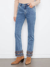 Load image into Gallery viewer, A person wearing light blue denim jeans with decorative multicolor embroidered trim at the cuffed hems, paired with tan ankle boots against a plain white wall.