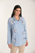 Load image into Gallery viewer, Woman wearing a light blue denim shirt with floral embroidery and tan pants on a white background.