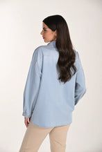 Load image into Gallery viewer, Woman wearing a light blue denim shirt and tan pants on a white background.