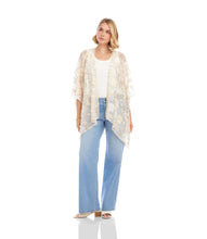 Load image into Gallery viewer, Woman wearing a floral gold and off-white kimono over a white top and blue jeans and white sandals standing against a white wall.