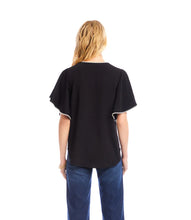 Load image into Gallery viewer, Woman wearing a black short sleeve blouse with cream trim and buttons and blue jeans against a white background.