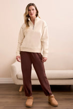 Load image into Gallery viewer, Woman wearing a moonstone zip up sweater, brown pants and brown shoes standing in a room with a beige couch.