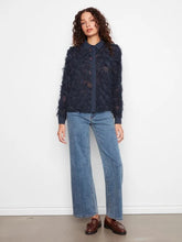 Load image into Gallery viewer, Woman modeling a navy blouse with fringe detailing, blue jeans and brown loafers against a white wall.