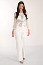 Load image into Gallery viewer, Woman wearing a white floral top, sparkly off -white jeans and silver sandals against a white background.