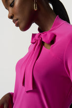 Load image into Gallery viewer, The Joseph Ribkoff long sleeve top features a slim silhouette, bow detail at the neckline, and an ultra-soft, stretchy fabric, allowing you to flaunt a feminine appearance. Ideal for wearing alone or for blending with a blazer, its design ensures a comfortable fit while elevating your look. Color- Opulence Fuchsia. Bow design detail at the neck. Keyhole neckline. Fabric -96% Polyester, 4% Spandex.
