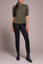 Load image into Gallery viewer, Woman wearing a spruce green short sleeve top, black pants and black boots against a neutral background.