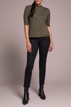 Load image into Gallery viewer, Woman wearing a spruce green short sleeve top, black pants and black boots against a neutral background.