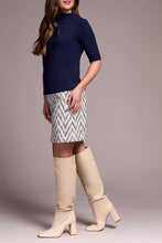 Load image into Gallery viewer, Woman wearing a navy top, patterned skirt, and beige knee-high boots against a neutral background.