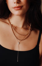 Load image into Gallery viewer, A close-up of a model wearing layered gold necklaces including a lariat necklace with teardrop and moonstone paired with a black top.