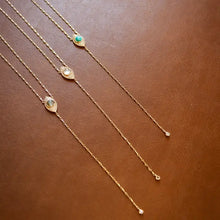 Load image into Gallery viewer, Three lariat necklaces with teardrops and each with a different gem in the center - labradorite, moonstone and turquoise lined up on a brown table.