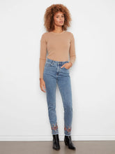 Load image into Gallery viewer, A woman with curly hair stands against a white wall wearing a brown long-sleeve top, blue jeans with floral embroidery at the hem and black boots.
