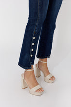 Load image into Gallery viewer, Model wearing dark blue jeans with decorative crystal buttons and beige sandals on a white background.
