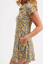 Load image into Gallery viewer, A woman wearing a short-sleeve collared dress with a yellow, black, and white floral pattern, shown from the side against a plain light background.