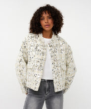 Load image into Gallery viewer, Woman wearing an off-white and silver sequin bomber jacket over a white top and grey jeans against a white background.