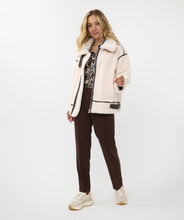 Load image into Gallery viewer, The luxurious Faux Fur Aviator Jacket in creamy ivory is a fashion statement. It boasts a plush faux fur exterior, complemented by dark brown leather accents and an elegant buckle detail for extra style. The inside is made of velvety suede that adds extra warmth. Designed with long sleeves and a zip-up closure, it's not only chic but also practical, ensuring warmth and fashion throughout the cooler seasons.