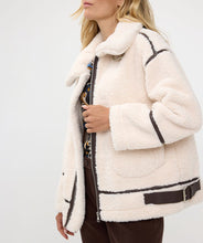Load image into Gallery viewer, The luxurious Faux Fur Aviator Jacket in creamy ivory is a fashion statement. It boasts a plush faux fur exterior, complemented by dark brown leather accents and an elegant buckle detail for extra style. The inside is made of velvety suede that adds extra warmth. Designed with long sleeves and a zip-up closure, it's not only chic but also practical, ensuring warmth and fashion throughout the cooler seasons.