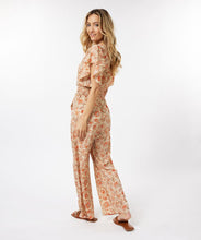 Load image into Gallery viewer, A breathtaking blend of orange, brown and red floral motifs on a pastel peach backdrop define the fashionable aura of the Tinslee jumpsuit. Delicate gold accents adorn the piece, accentuating the visual appeal of the design. For added drama, it features ruffled sleeves and an elasticized waist with tassels to give it a captivating, effortless style. Color- Orange, brown, red, pastel peach, gold. One piece. Elasticized waist with tassels. V-neck. Ruffle sleeves. Fabric- 100% Polyester.