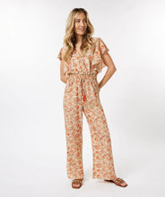 Load image into Gallery viewer, A breathtaking blend of orange, brown and red floral motifs on a pastel peach backdrop define the fashionable aura of the Tinslee jumpsuit. Delicate gold accents adorn the piece, accentuating the visual appeal of the design. For added drama, it features ruffled sleeves and an elasticized waist with tassels to give it a captivating, effortless style. Color- Orange, brown, red, pastel peach, gold. One piece. Elasticized waist with tassels. V-neck. Ruffle sleeves. Fabric- 100% Polyester.