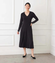 Load image into Gallery viewer, Woman in a long black dress with crystal embellishments on the sleeves and black heels standing in a room with a white wall.