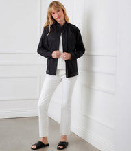 Load image into Gallery viewer, Woman wearing a black blouse over a white top and white pants and black sandals against a white paneled wall.