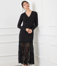 Load image into Gallery viewer, Woman wearing a black dress with a lace bottom leaning against a white wall.