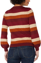 Load image into Gallery viewer, Model wearing burgundy multicolor striped crewneck sweater and blue jeans against a white background.