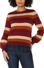 Load image into Gallery viewer, Model wearing burgundy multicolor striped crewneck sweater and blue jeans against a white background.