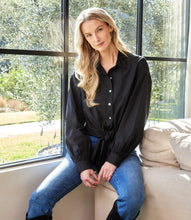 Load image into Gallery viewer, Woman wearing a long sleeve black shirt with a tie waist, blue jeans and black boots sitting on a couch in front of large windows with a view of a yard.