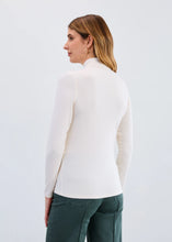 Load image into Gallery viewer, Woman wearing a cream mock neck top and green jeans against a plain background.