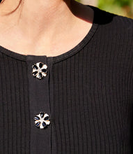 Load image into Gallery viewer, Close-up of a black top with floral buttons on a blurred natural background.