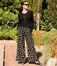 Load image into Gallery viewer, Woman wearing a black long sleeve top with floral pants, sunglasses and black sandals in an outdoor setting.