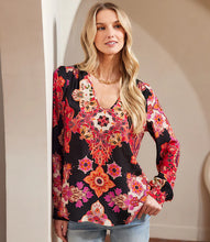 Load image into Gallery viewer, Woman wearing a colorful floral blouse, gold necklace and jeans against a neutral setting.