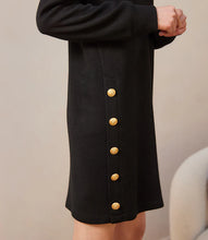 Load image into Gallery viewer, Close up of model wearing black dress and gold button detailing against a white background.