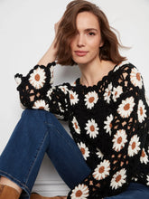 Load image into Gallery viewer, A woman wearing a black crochet knit sweater with large white daisy flower patterns and blue jeans, posed against a light gray wall.