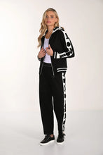 Load image into Gallery viewer, Woman wearing a black and white tracksuit and black tennis shoes with a white background.