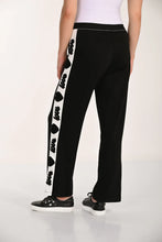 Load image into Gallery viewer, Woman wearing a black pant with white contrast stripe and black hearts and word love and black tennis shoes against a white background.