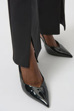 Load image into Gallery viewer, Close-up of black lux pants with front slits and black patent heels against light background.