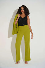 Load image into Gallery viewer, Woman wearing a sparkling black top, green pants and strappy heels, holding a green jacket against a white background.