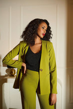 Load image into Gallery viewer, Woman wearing a green suit and sparkling black top standing against a white wall.