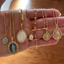 Load image into Gallery viewer, Model holding several gold religious symbol pendant necklaces against a blurred brown background.