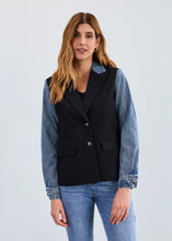 Load image into Gallery viewer, Woman wearing a black blazer with denim sleeves and collar and blue jeans against a plain background.