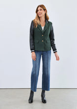 Load image into Gallery viewer, Woman wearing a green blazer with black sleeves, white shirt, blue jeans, and black boots against a white background.