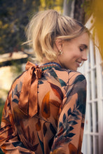 Load image into Gallery viewer, Woman wearing gold earrings, a leaf patterned blouse with a gold bow tie, standing outdoors.