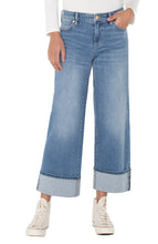 Load image into Gallery viewer, Model wearing cuffed blue jeans, white top and white high-top sneakers.